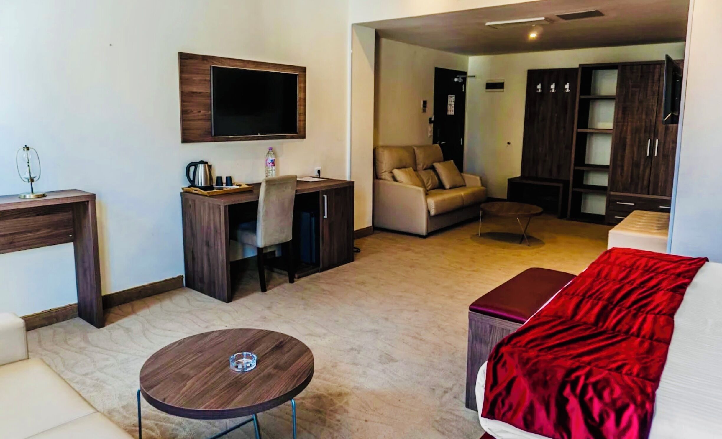 A modern living room with a flat-screen TV, a sofa, a coffee table, and a red ottoman.