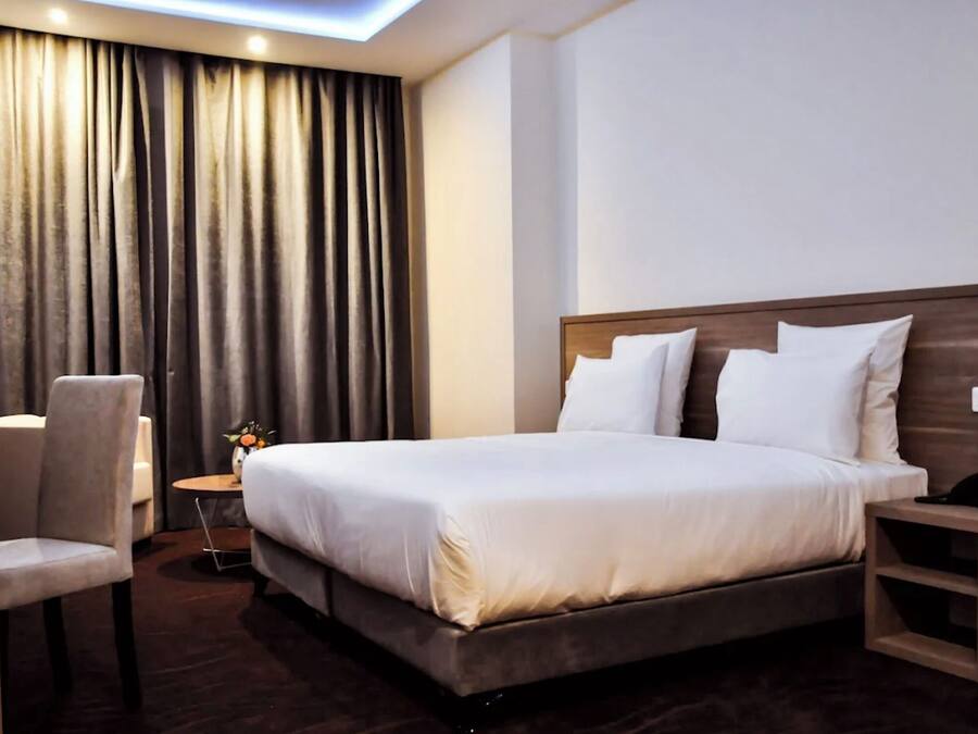 Una habitación de hotel con cama, escritorio, silla y una mesita con un jarrón de flores.