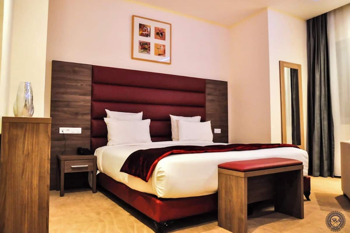 Une chambre d’hôtel avec un grand lit, une table de chevet, une commode et un banc en bois.