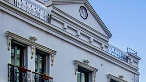 Un hotel de varios pisos con balcones, un reloj en la fachada y un letrero en un idioma extranjero.