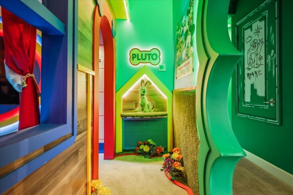 Un pasillo colorido con un letrero de neón que dice 'PLUTO', una pared verde con una ventana y una puerta con un dibujo.