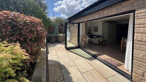 A patio with a glass door leading to a living area, surrounded by a brick wall and greenery. - Havendale (Chesterfield)