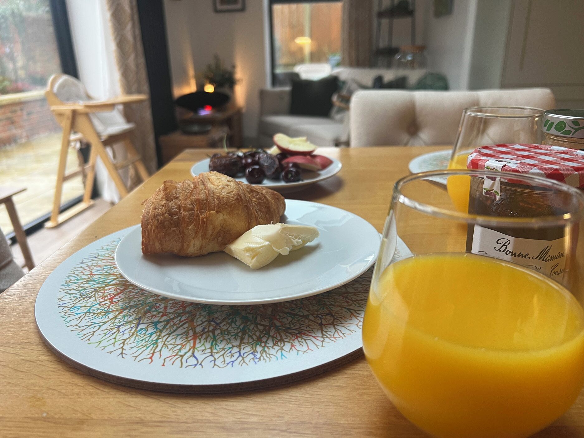 A breakfast setting with croissant, butter, and orange juice on a table.