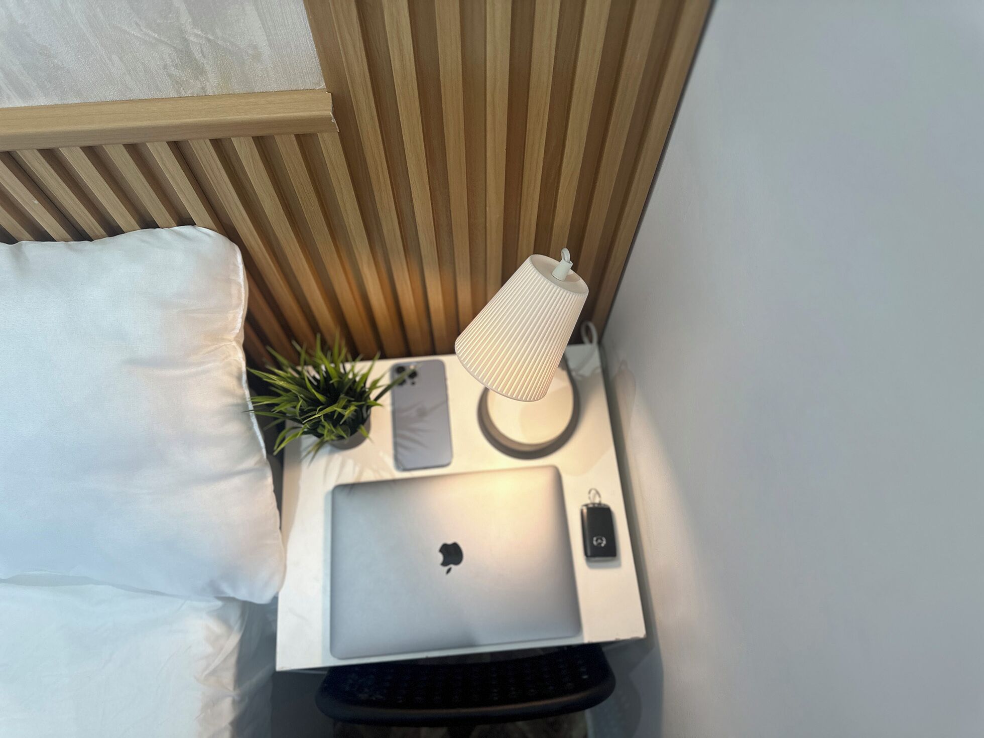 Een klein nachtkastje met een laptop, een lamp, een plant en een afstandsbediening.