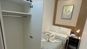 A bedroom with a bed, a wardrobe, a nightstand, a lamp, and a wall-mounted picture. - Beautiful Partition Room in Tecom (Dubai)