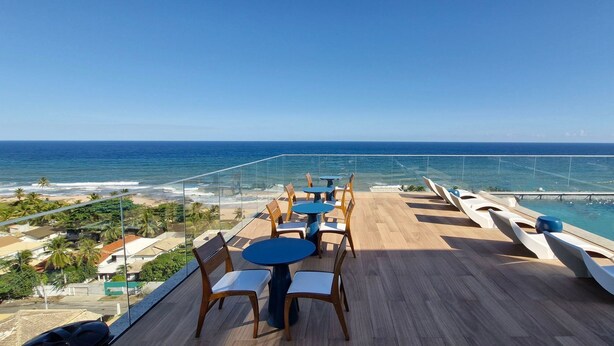 A deck with tables and chairs overlooking a pool and ocean view. - COPDS0110 - Pedra do Sal Privilege (Salvador)