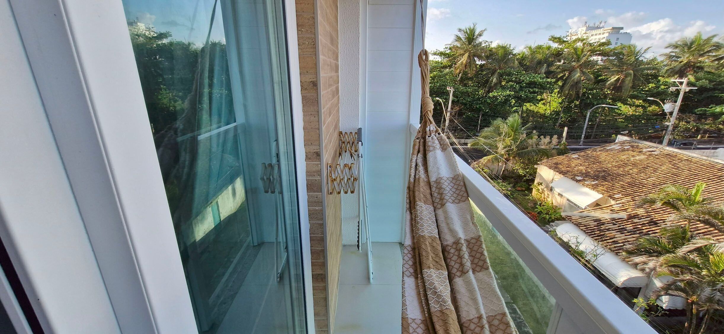 A balcony with a view of a residential area, including a tiled roof and palm trees.