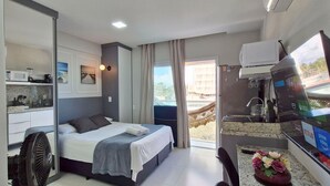 A modern hotel room with a bed, a small kitchenette, a TV, and a balcony with a view. - COPDS0110 - Pedra do Sal Privilege (Salvador)