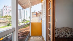 Un balcon donnant sur les immeubles de la ville, une porte en bois et un lit recouvert d’une courtepointe à motifs floraux.