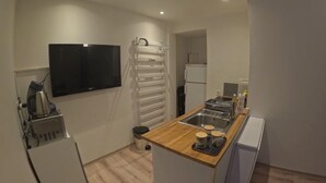 A compact kitchen with a wooden countertop, a built-in sink, a refrigerator, and a wall-mounted TV. - Studio "A deux pas des thermes" in the heart of Uriage park. (Saint-Martin-d'Uriage)