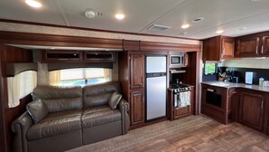 Cocina compacta para autocaravana con refrigerador, microondas, estufa y un pequeño comedor.