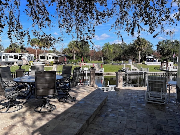 An outdoor patio with tables and chairs, a small pond, and RVs in the background. - GLAMPING at its finest. Water front, shaded, private dock, river and lake access (Lake Wales)