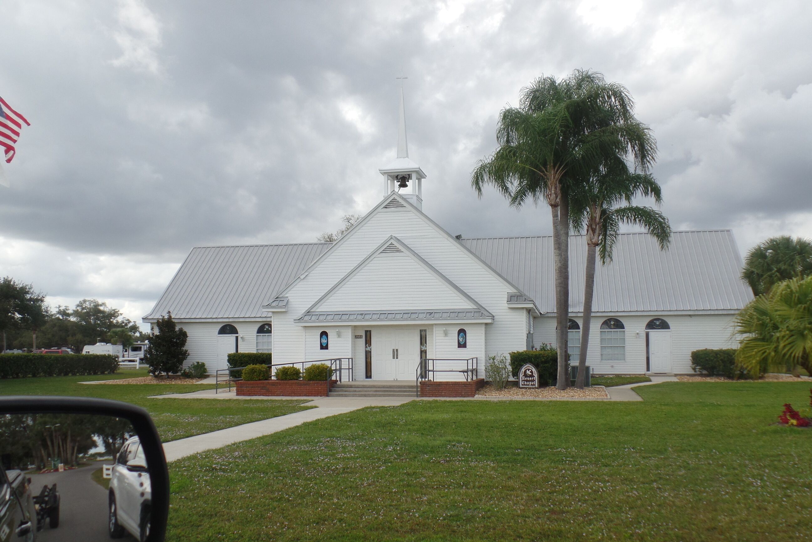 A white church with a bell tower, surrounded by a well-maintained lawn and palm trees.