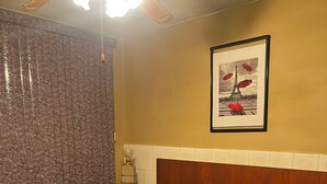 A bedroom with a bed, a nightstand, a ceiling fan, a framed picture of the Eiffel Tower, and a curtain.