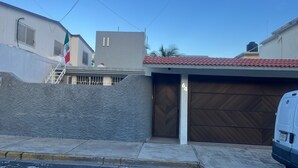 A residential garage with a metal door, a white van parked outside, and a flag on a building.