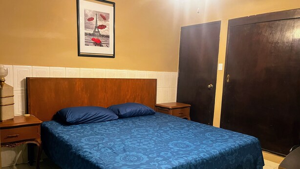 A bedroom with a bed, a nightstand, a dresser, a wardrobe, and a framed picture on the wall.