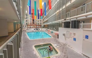 An indoor swimming pool area with a hot tub and a smaller pool, surrounded by a high-ceilinged corridor with balconies. - Bubbles Up! Cozy condo in a perfect oceanfront location with amazing amenities (Myrtle Beach)