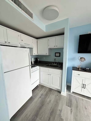A compact kitchen with white cabinets, a built-in stove, and a sink. - Bubbles Up! Cozy condo in a perfect oceanfront location with amazing amenities (Myrtle Beach)