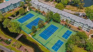 Ovenfra ses et hotel med flere tennisbaner, en flod og grøn bevoksning omkring.