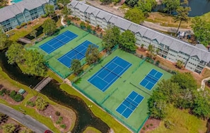 Eine Vogelperspektive auf ein Hotel mit mehreren Tennisplätzen, einem Fluss und umgebender Grünfläche.