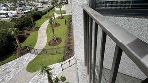 En høj bygning med balkon, udsigt over anlagt område med palmer og parkeringsplads.