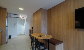 Cozinha moderna com parede de madeira, mesa redonda com cadeiras, um banco, TV montada na parede e uma placa indicando a saída.