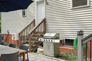 Un patio al aire libre con una mesa y sillas de madera, una parrilla y un tanque de propano.