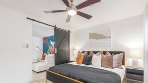 Une chambre à coucher moderne avec un lit, un ventilateur de plafond, une porte coulissante, un canapé blanc et une table de chevet.