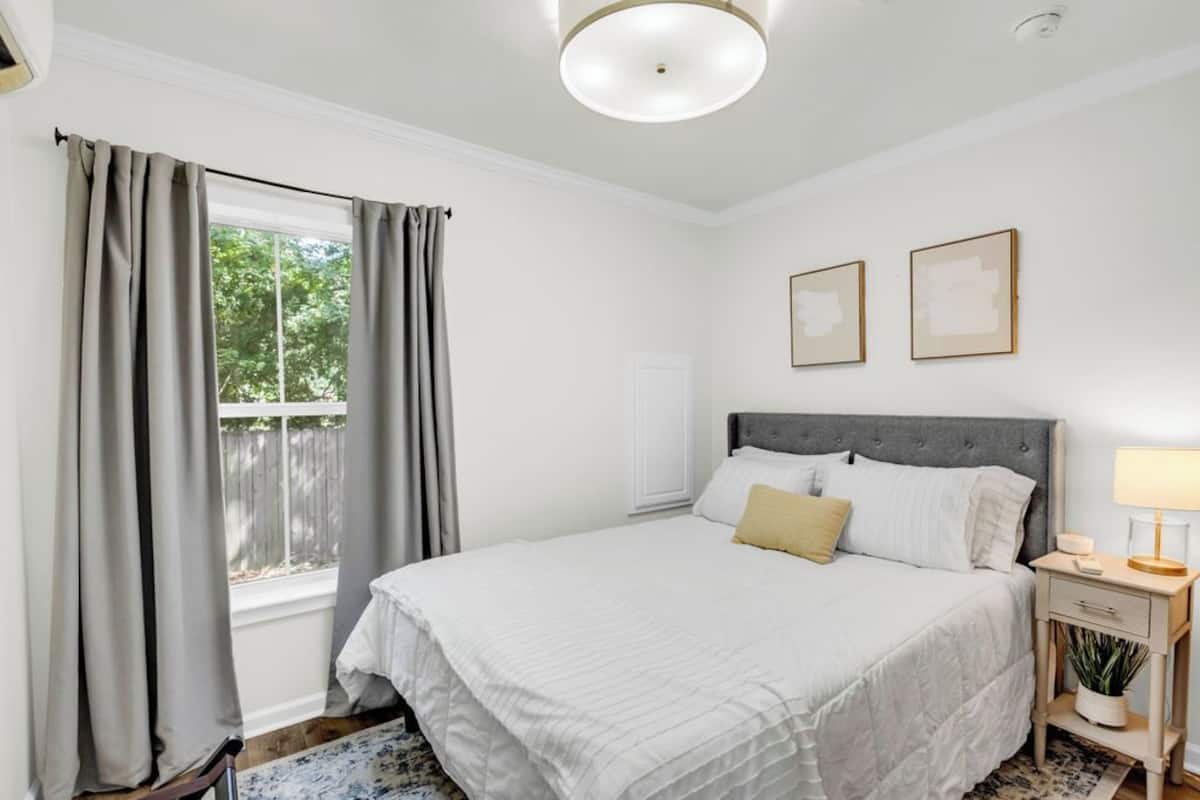 Een slaapkamer met een groot bed, een nachtkastje met een lamp en een raam met gordijnen.