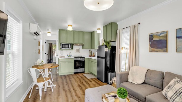 Eine moderne Küche mit grünen Schränken, ein Essbereich mit weißen Stühlen und ein graues Sofa.