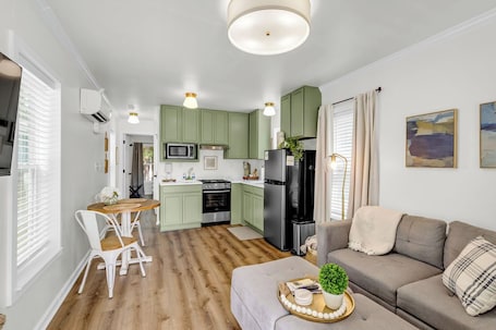 A modern kitchen with green cabinets, a dining area with white chairs, and a grey sofa.