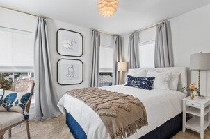Un dormitorio con una cama grande, una mesita de noche con lámpara y una silla con cojín.