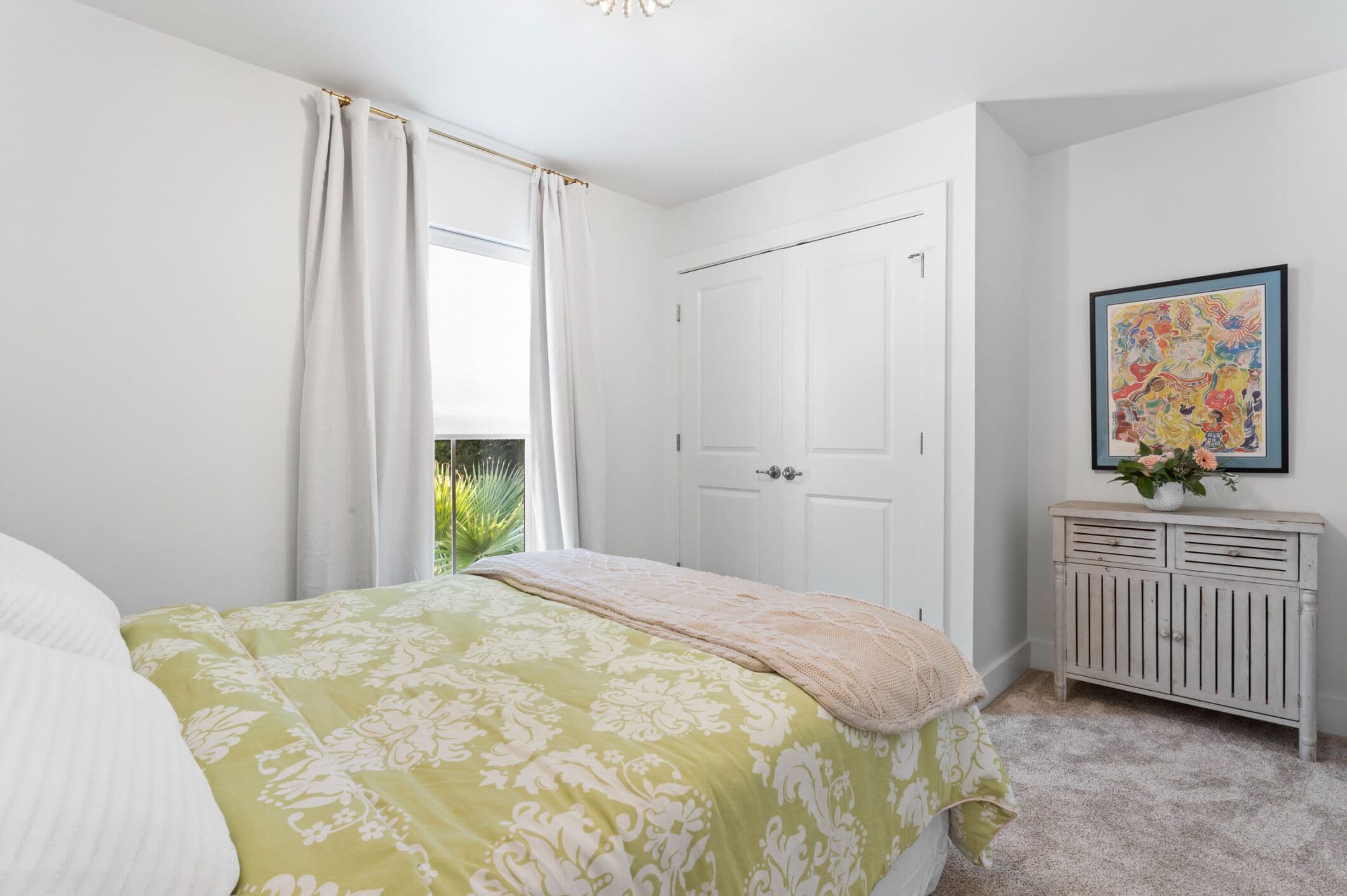 A bedroom with a bed, a wardrobe, a window with curtains, and a painting on the wall.