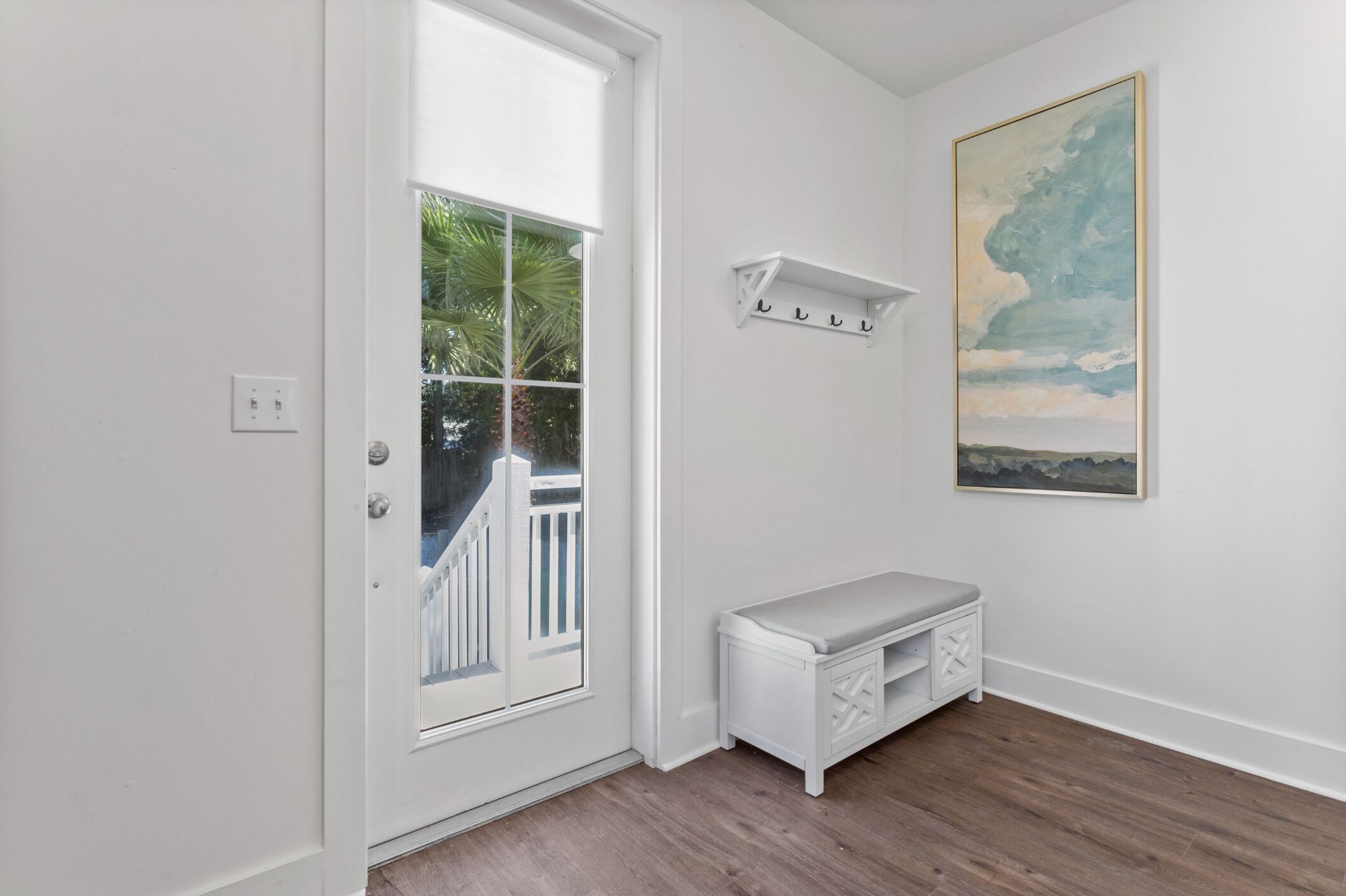 A hallway with a white door, a bench, a wall-mounted shelf, and a painting.