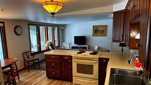 A kitchen with wooden cabinets, a stove, a sink, and a dining area with chairs. - Foster's Lakeside - Sandy Shore with Snowmobile Access & Year-Round Fun (Tomahawk)