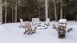 A snow-covered outdoor seating area with Adirondack chairs and a fire pit in a forest. - Catskills Mountain Home Near Windham w/ Fireplace & Open Living Deer Run Lodge by Avantstay (Prattsville)