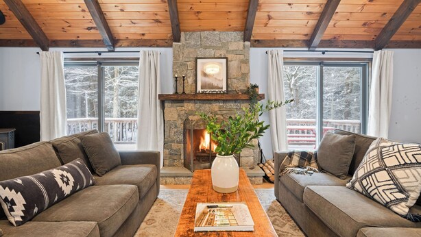 A cozy living room with a stone fireplace, two sofas, a coffee table, and large windows with a view of trees. - Catskills Mountain Home Near Windham w/ Fireplace & Open Living Deer Run Lodge by Avantstay (Prattsville)