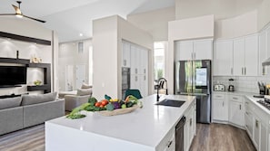 A modern kitchen with white cabinetry, a stainless steel refrigerator, and a central island with a fruit bowl. - Private Pool, Chefs Kitchen & Patio Near Old Town Scottsdale Desert Luma by Avantstay (Scottsdale)