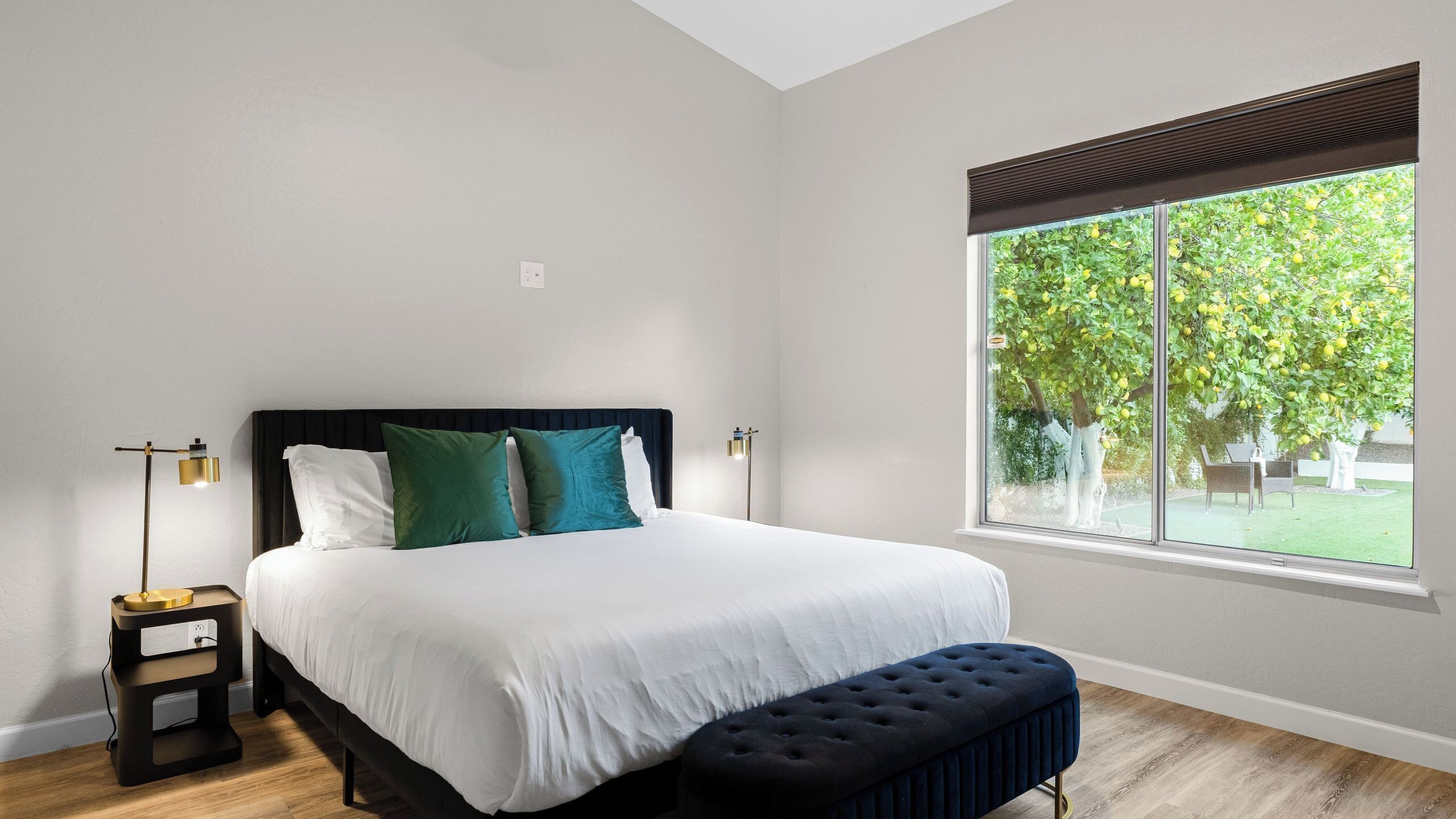 Un dormitorio con una cama grande, dos mesitas de noche, un banco y una ventana con vistas a un árbol.