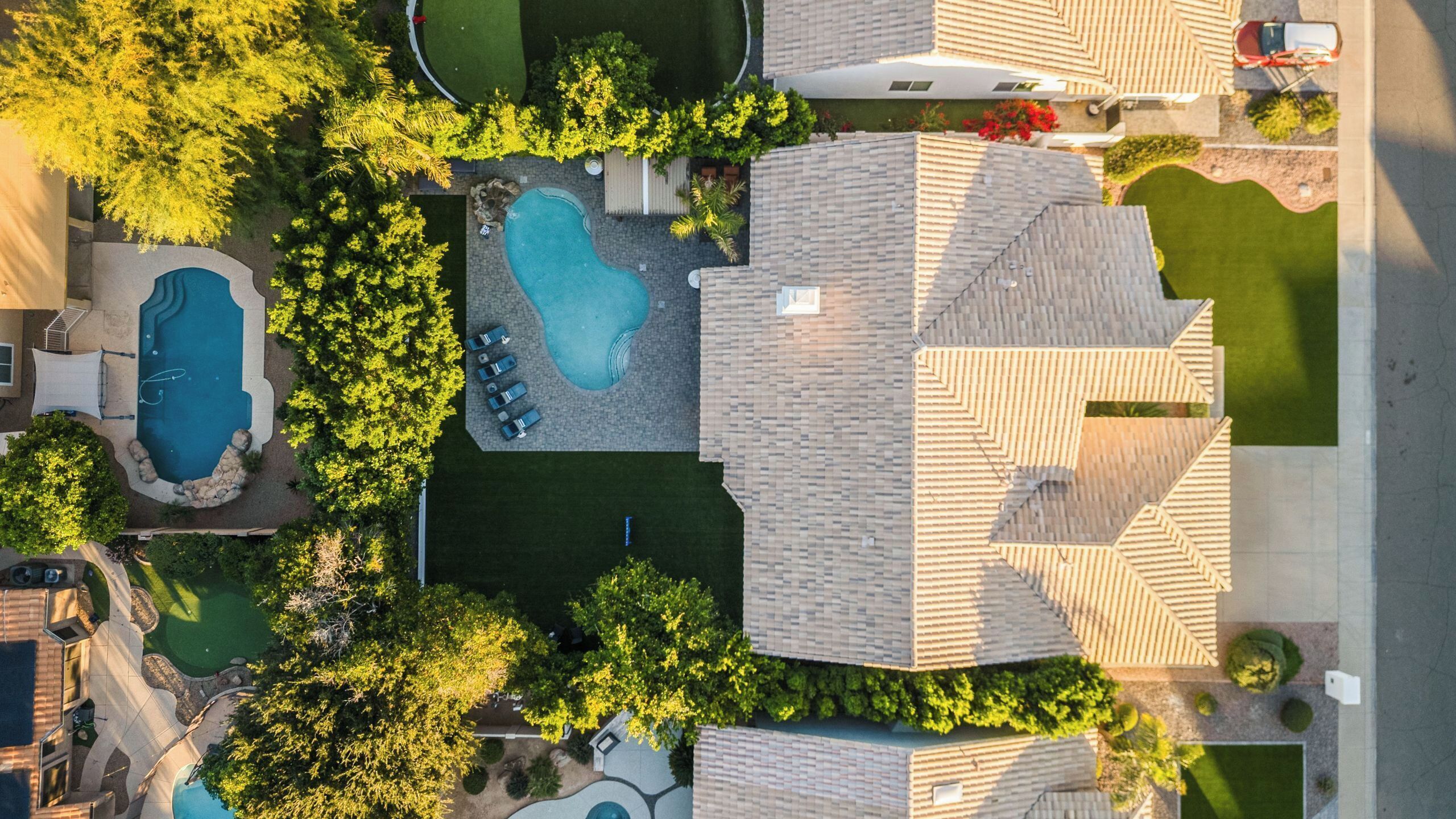 Vue aérienne d’un quartier résidentiel avec une piscine, un court de tennis et une maison dont le toit présente un design original.