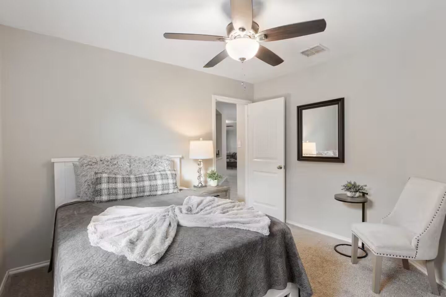 Un dormitorio con cama, una silla, ventilador de techo, lámpara y espejo.