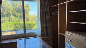A room with a large window, wooden cabinets, and a glass-top desk.