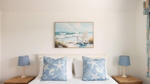 Una camera da letto con un letto, due comodini e un quadro raffigurante una spiaggia sopra il letto.