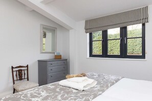 Una camera da letto con un letto, una cassettiera, una sedia, una finestra con tenda a righe e uno specchio appeso al muro.