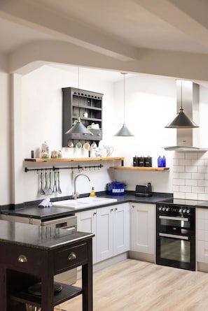 Una cocina moderna con armarios blancos, encimera negra, horno integrado y utensilios colgantes.