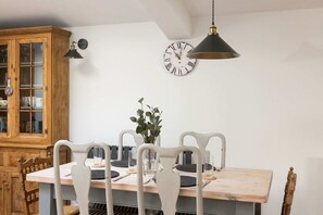 A dining area with a wooden table, white chairs, a clock, and a pendant light. - Sidlesham Hideaway Logburner Garden (Chichester)