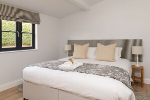 A neatly made bed with a striped headboard, two bedside lamps, and a window with a striped valance. - Sidlesham Hideaway Logburner Garden (Chichester)
