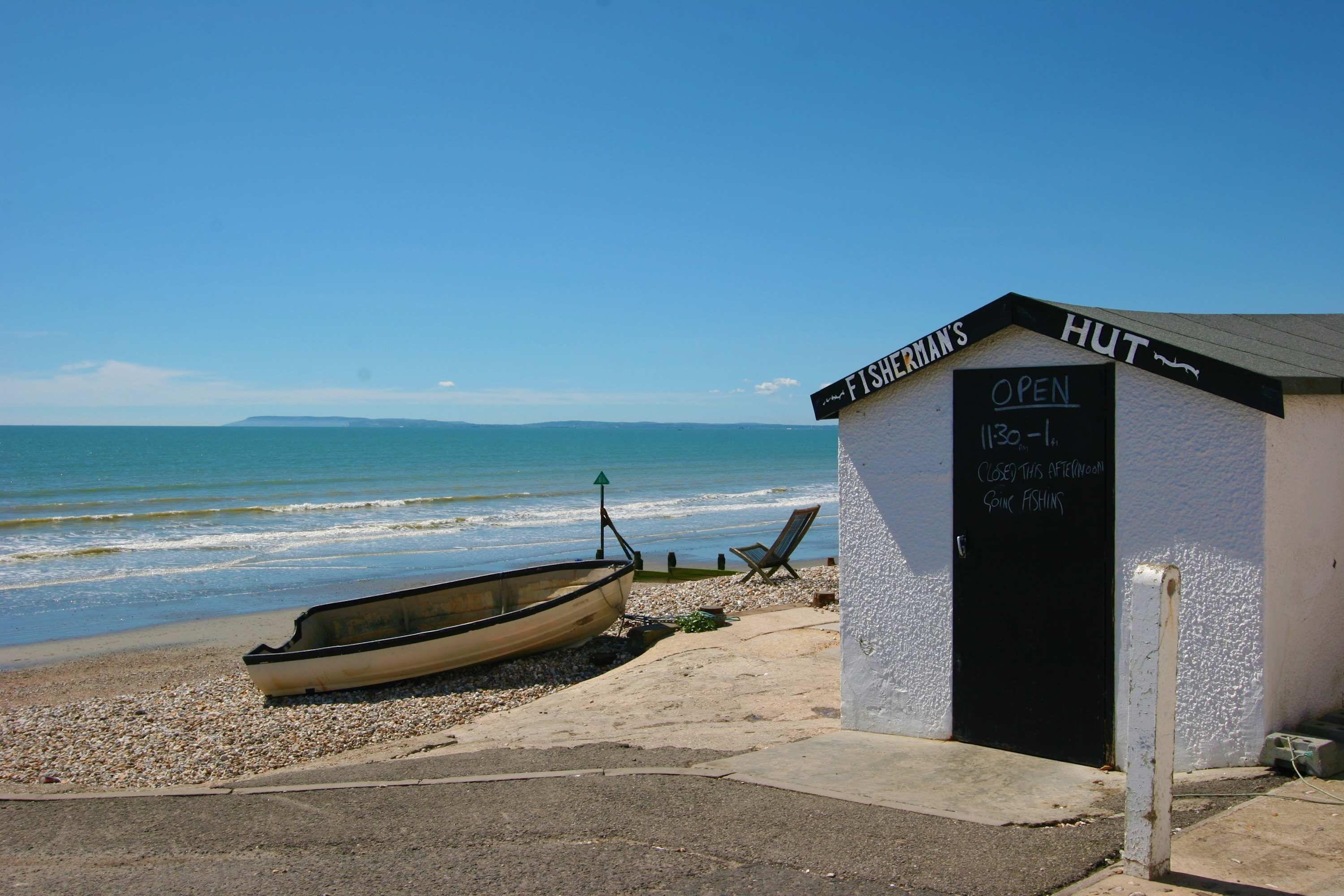 A small white building with a black door labeled "FISHERMAN'S HUT" and a sign indicating it's open from 11:30 to 1.