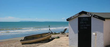 Un pequeño edificio blanco con una puerta negra con la leyenda 'FISHERMAN'S HUT' y un letrero que indica que está abierto de 11:30 a 1.