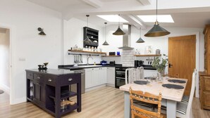 Et moderne køkken med hvide skabe, en mørk træø, hængende lys og et spiseområde med et bord dækket til to personer.